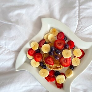 A white plate with pancakes topped with sliced bananas, strawberries, and blueberries.