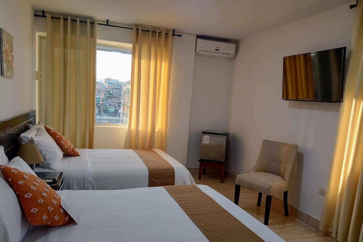 A hotel room with two beds, a TV, a desk, and a chair.
