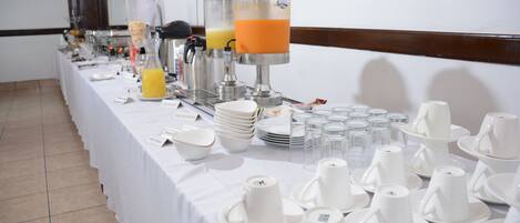 A buffet setup with various food items and beverages, including a juice dispenser and plates.