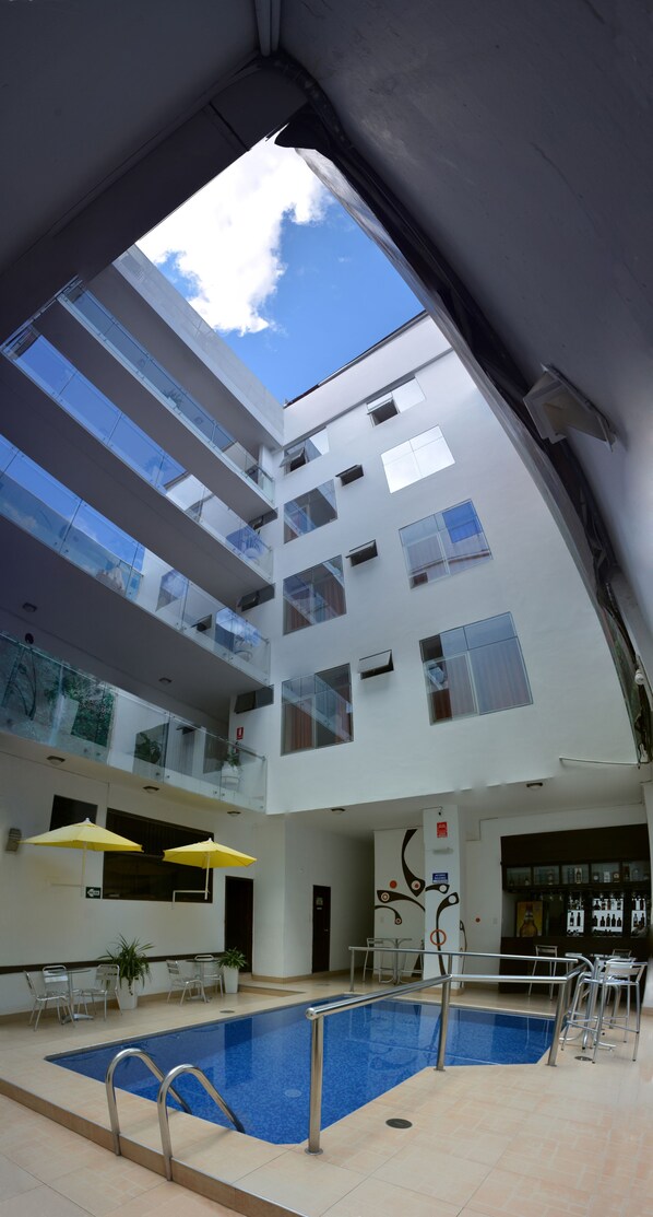 A modern building with a central swimming pool, multiple balconies, and a clear view of the sky.