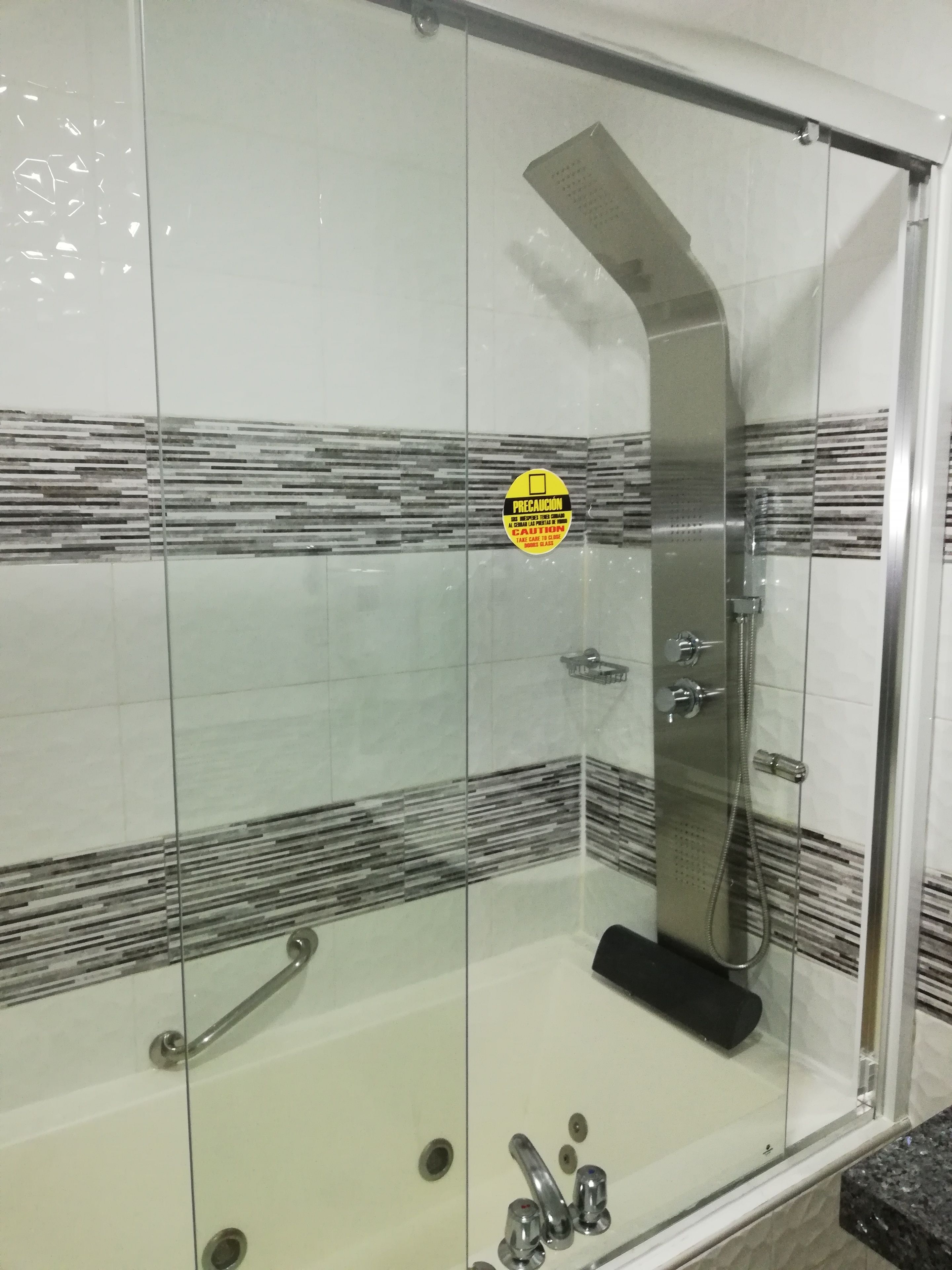 A glass-enclosed shower stall with a curved showerhead, a handheld showerhead, and a control panel.