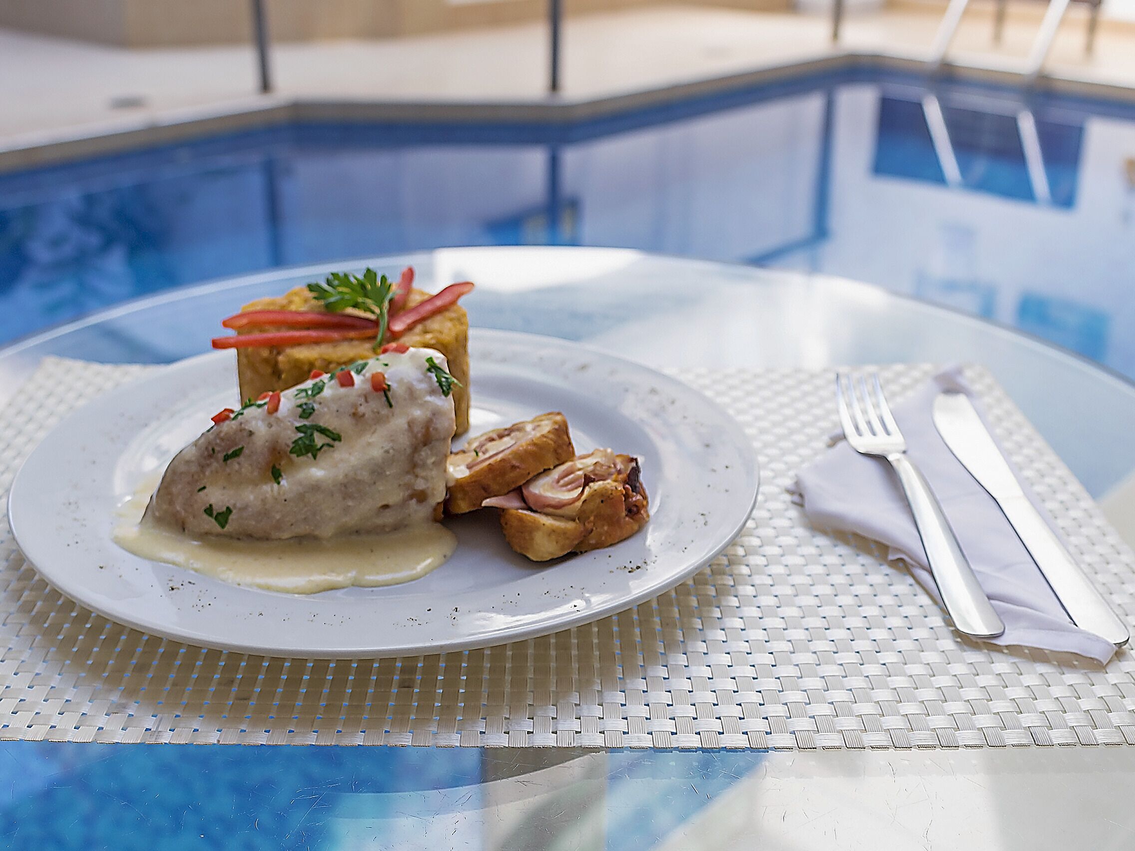 Un plato con comida, un tenedor y un cuchillo sobre una mesa cerca de una piscina.