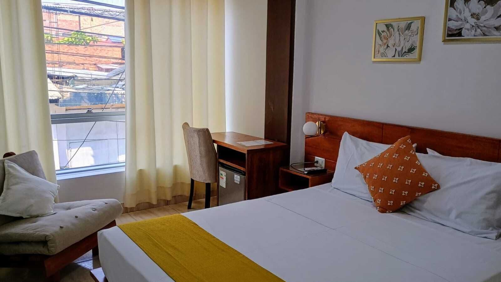 A hotel room with a bed, a desk, a chair, and a window with curtains.