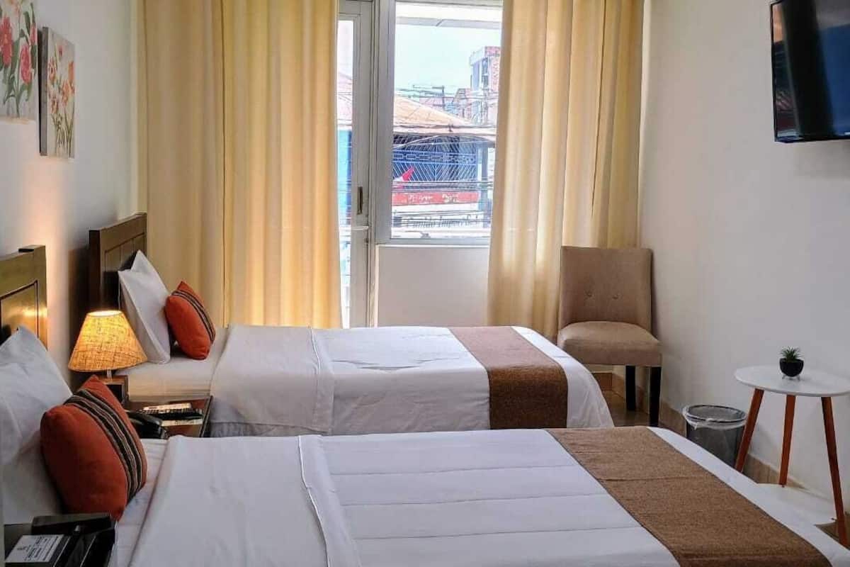 A hotel room with two beds, a chair, a small table with a plant, and a TV mounted on the wall.
