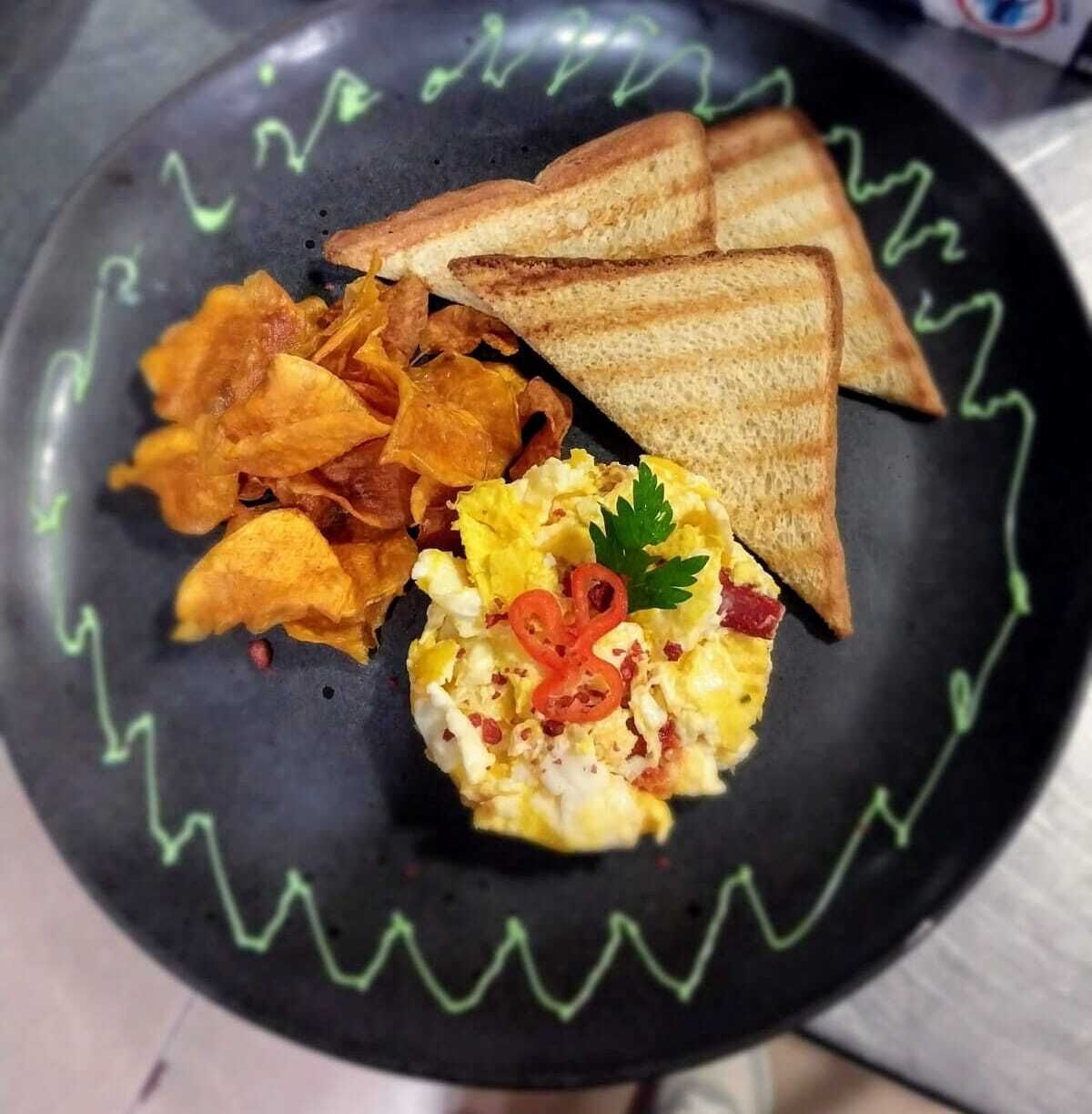 A plate with scrambled eggs, toast, and chips.