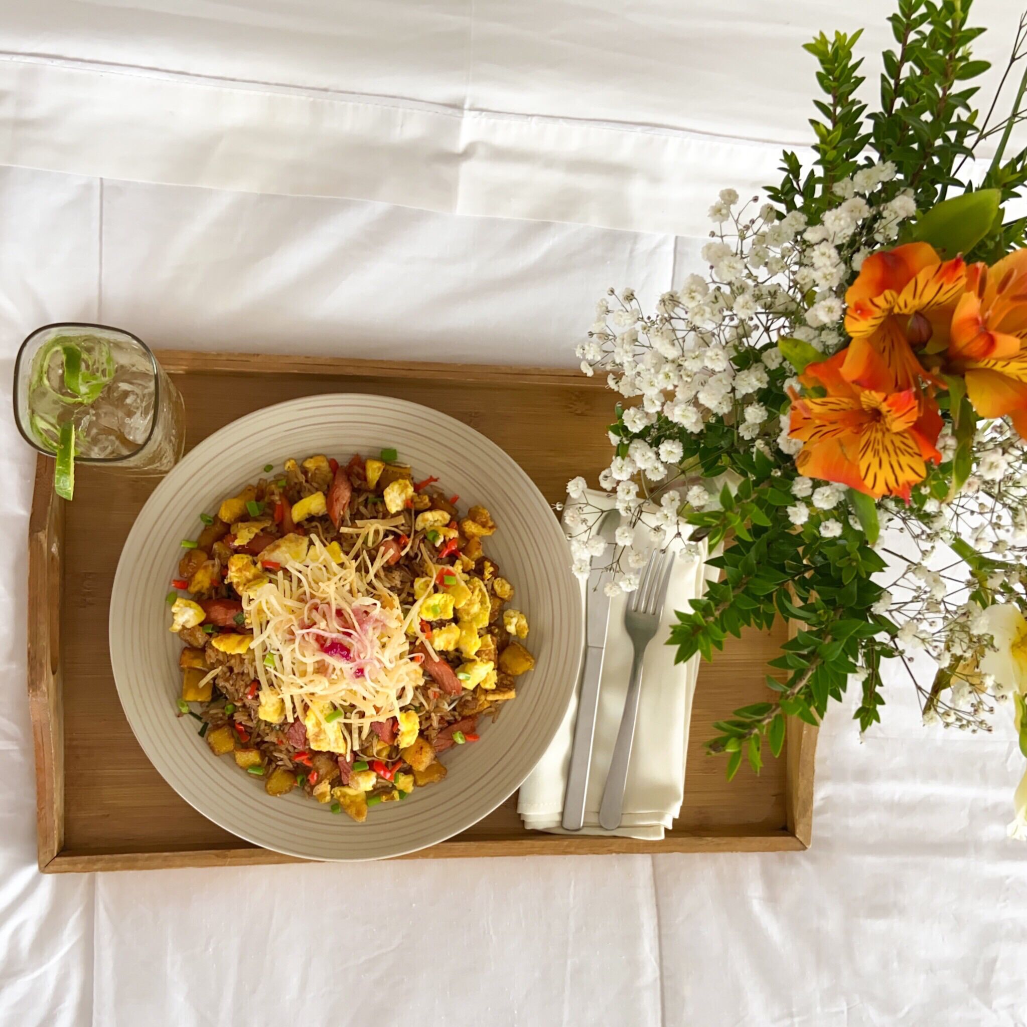 A tray with a plate of food, a glass of drink, and a floral arrangement.