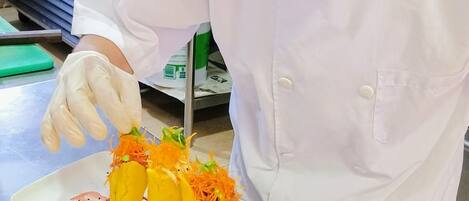 Een kok in een witte uniform en koksmuts bereidt eten op een roestvrijstalen toonbank.