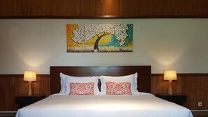 Een groot bed met witte lakens, twee rode kussens met dessin en twee bedlampen.