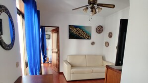 Una sala de estar con un sofá beige, un ventilador de techo y un televisor sobre un mueble de madera.