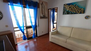 Una sala de estar con un sofá color beige, una zona de comedor con muebles de mimbre y un cuadro de peces en la pared.