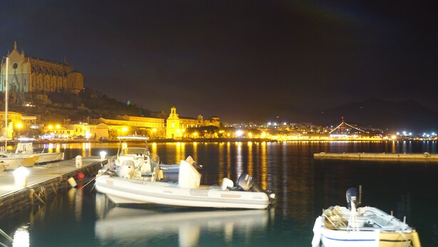A nighttime harbor with boats docked, a prominent building with lights, and a bridge in the background. - Surrounded by greenery near the sea (Rosa cottage) (SPIGNO SATURNIA)