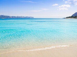 Une plage de sable fin bordée d’une eau turquoise et dominée par des montagnes lointaines.