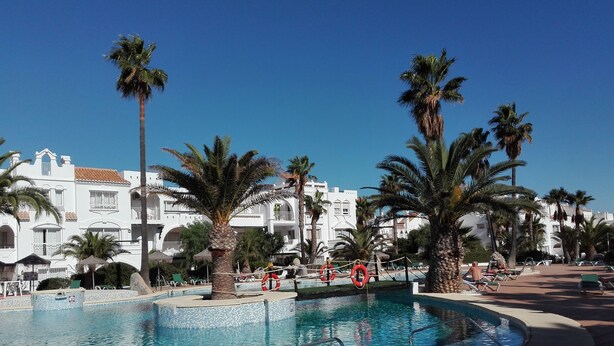 A pool area with palm trees, lounge chairs, and a building with balconies. - The Blue Pearl, a dream terrace in the sun (Roquetas de Mar)