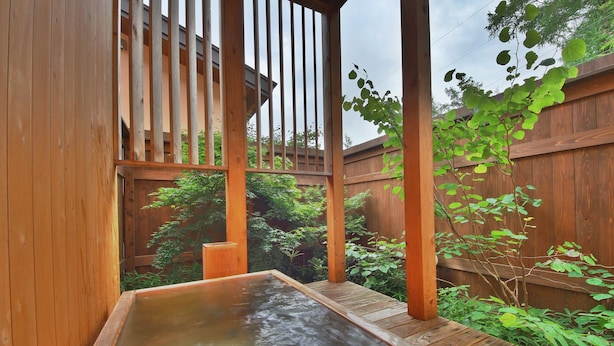 A wooden hot tub area with a wooden deck and a wooden fence in the background. - One More Time Heart (Nikko)