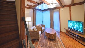 A living room with a wooden staircase, a television, wicker furniture, and a patterned rug. - One More Time Heart (Nikko)
