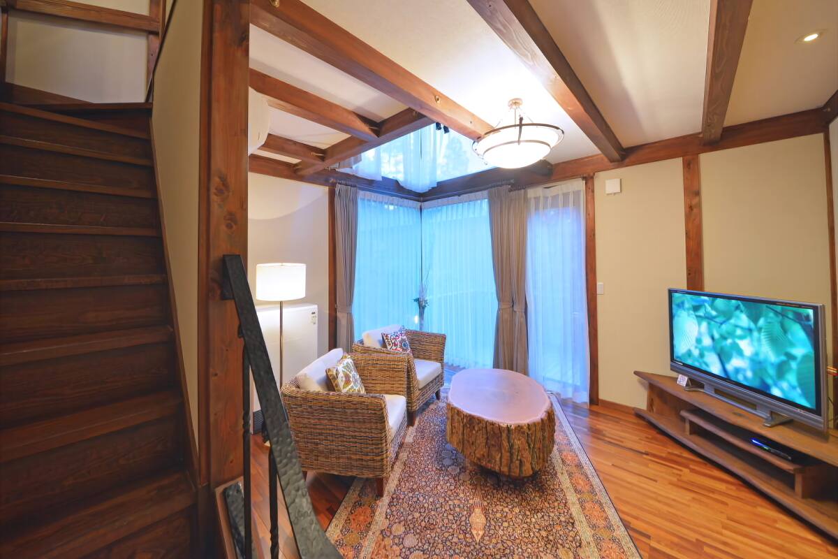 A living room with a wooden staircase, a television, wicker furniture, and a patterned rug.