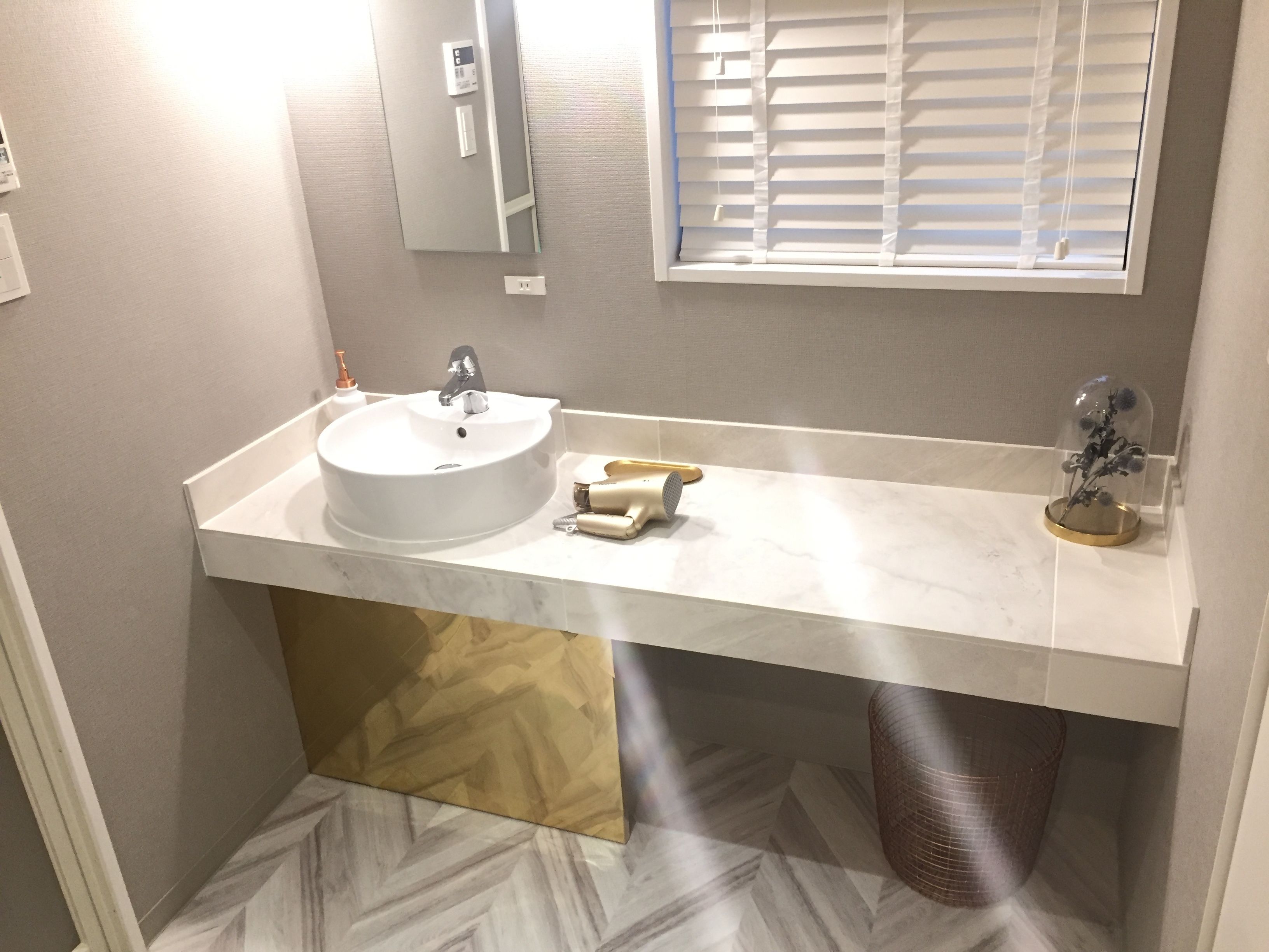 A bathroom with a white sink, a mirror, a window with blinds, and a shower area.