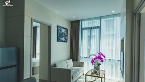 Una habitación de hotel moderna con sofá, una mesa de comedor, una mesa de centro y un ventanal con cortinas.