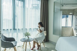 A hotel room with a bed, a sitting area with a chair and a small table, a potted plant, and a large window with curtains. - TD Central Hotel & Apartment (Ho Chi Minh City)