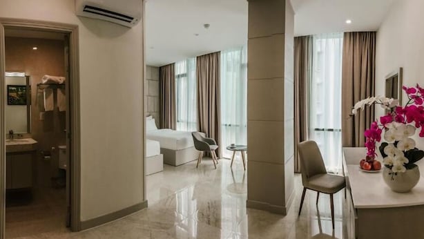 Una habitación de hotel moderna con baño, una sala de estar con sofá y sillones, y un comedor con mesa y sillas.