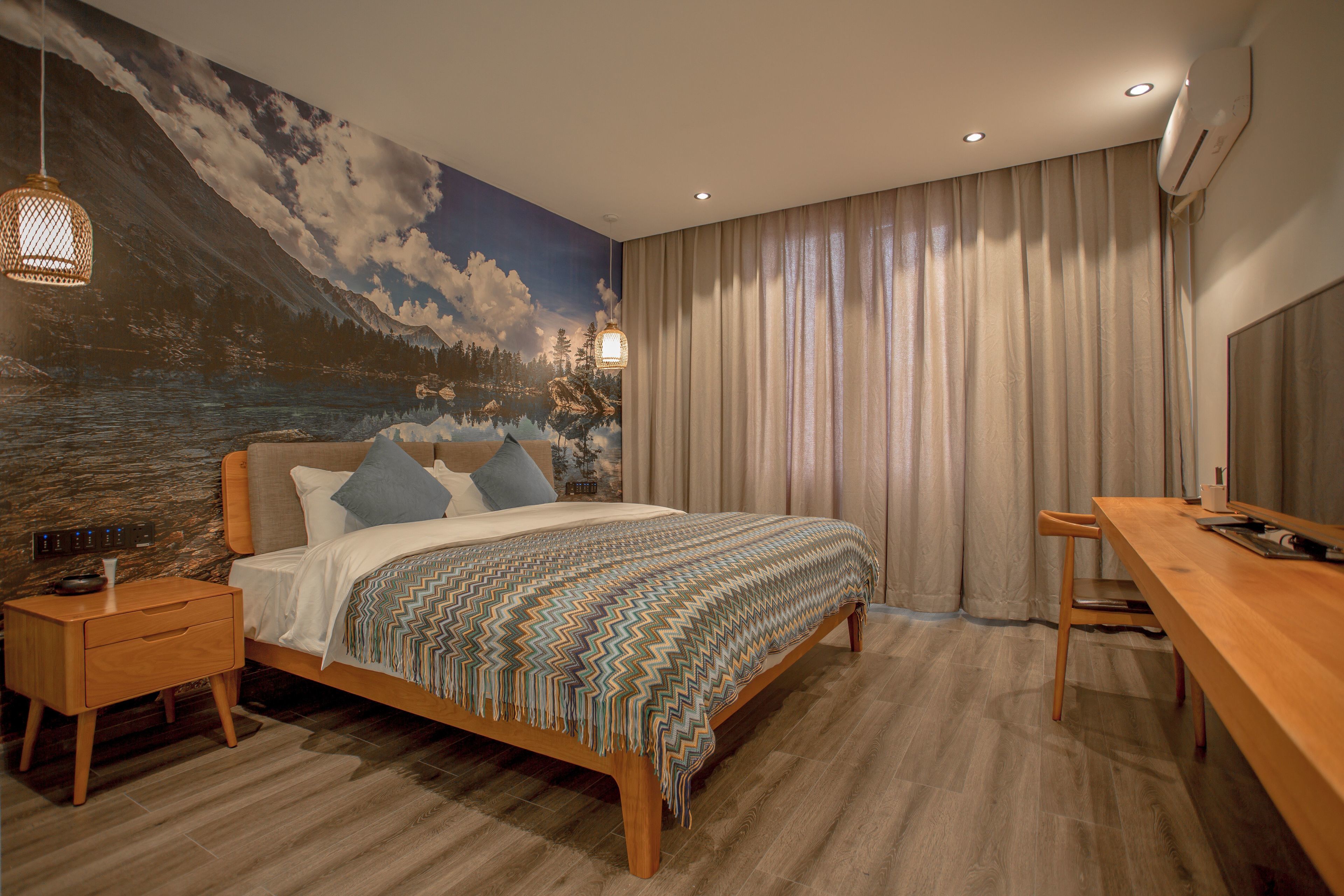 A bedroom with a bed, a nightstand, a desk, and a mural on the wall.