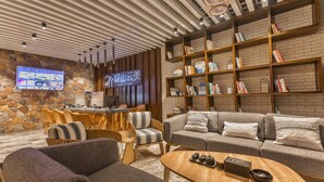 A modern hotel lobby with a stone wall, wooden furniture, a flat-screen TV, and a bookshelf. - Purmei Hotel Lugu Lake (Lijiang)