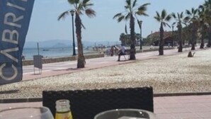 A table with drinks and a bottle, a flag, and a beach in the background.