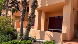 A building with a beige facade, palm trees, and a red shuttered window.