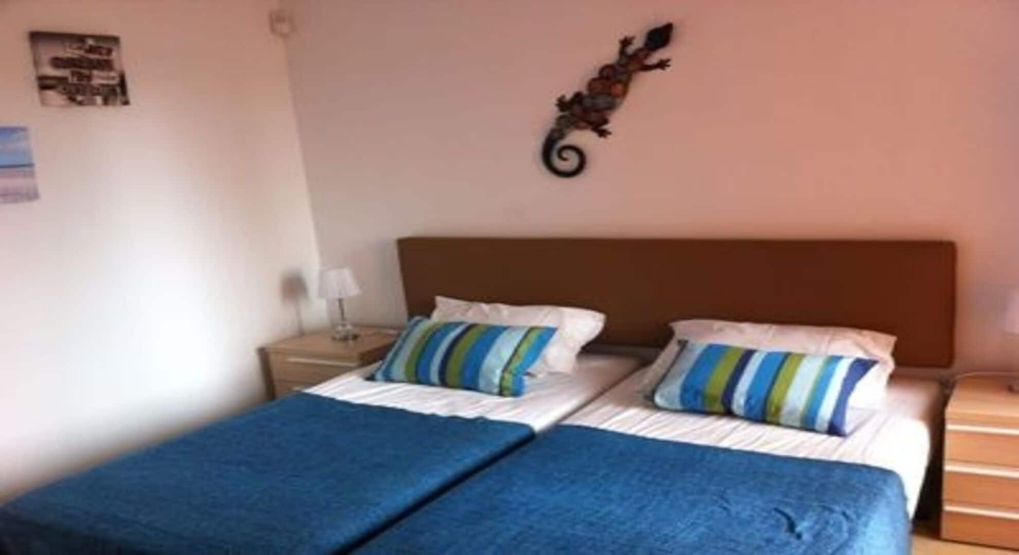 A double bed with two pillows, a nightstand with a lamp, and a decorative wall piece.