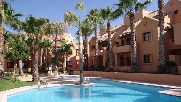A swimming pool surrounded by palm trees and beige buildings with balconies.