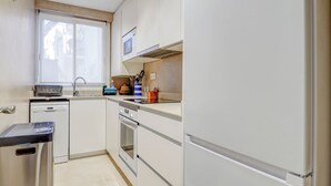 Une cuisine de taille réduite, avec des meubles blancs, un four à micro-ondes, un lave-vaisselle et une cuisinière.