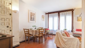 Un salon confortable avec un canapé, une table à manger et des chaises, ainsi qu’une fenêtre avec des rideaux.