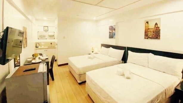 A hotel room with two beds, a desk, and a TV. - Pension Inn Marilao (Marilao)