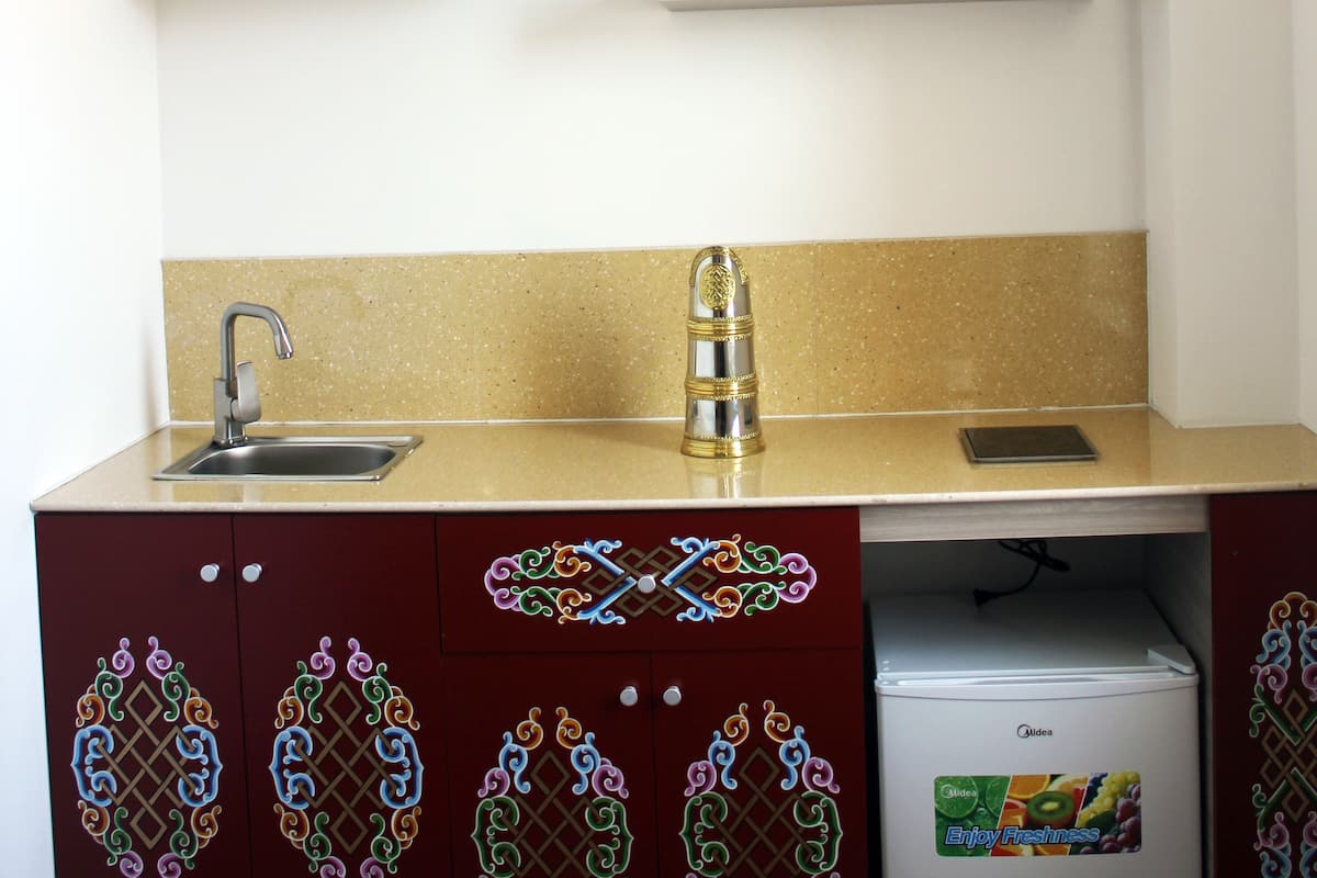 A kitchenette with a stainless steel sink, a microwave, and a small refrigerator. There are wooden shelves above the counter and a decorative backsplash.