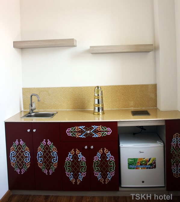 A kitchenette with a stainless steel sink, a microwave, and a small refrigerator. There are wooden shelves above the counter and a decorative backsplash. - Tsetsen Khangai Hotel (Ulaanbaatar)