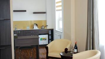 A compact kitchen with a refrigerator, sink, and bar area. There is a chair and a small table with wine glasses and a bottle.