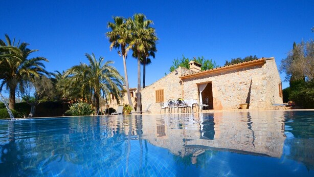 A clear blue pool with a stone building in the background, palm trees, and a clear sky.