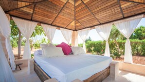 A bed with white bedding and a pink pillow, under a wooden ceiling with white curtains.