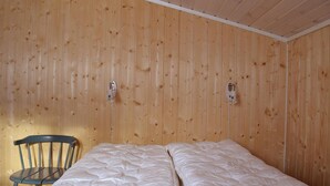 A room with wooden walls, a single bed with white bedding, and a chair.