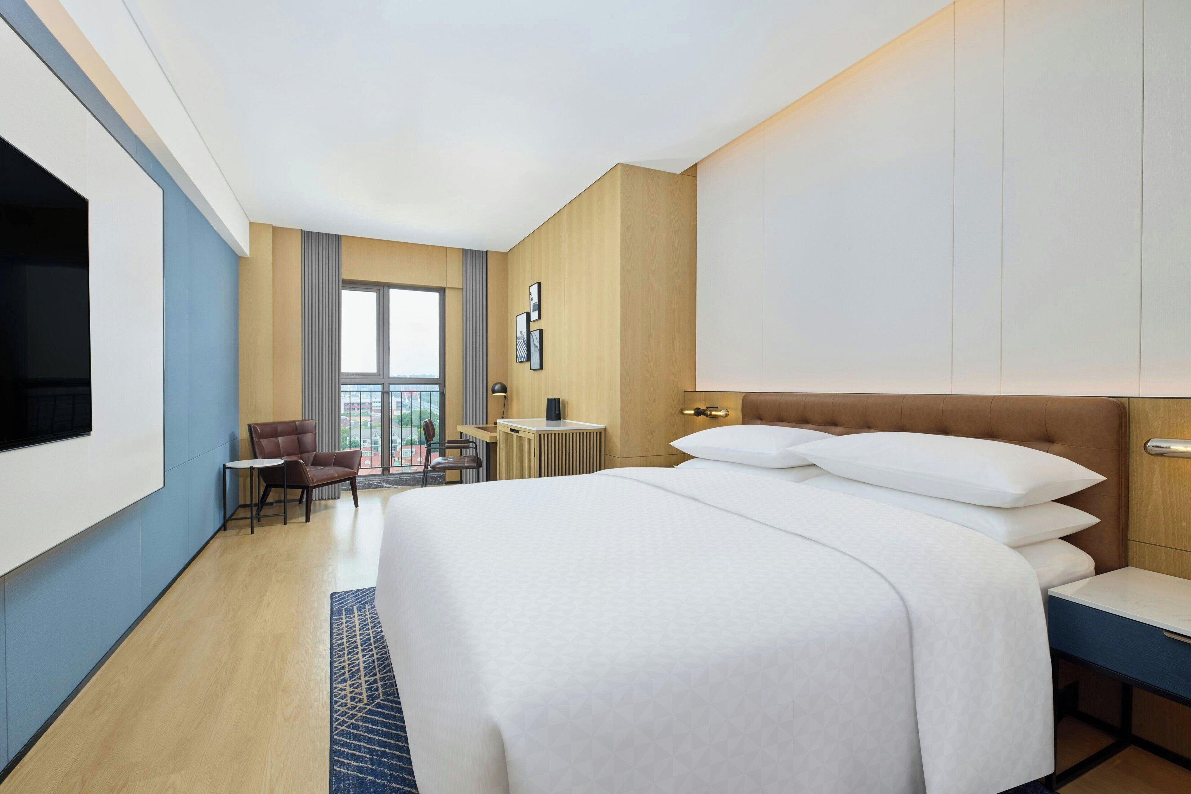 A modern hotel room with a large bed, a desk, a chair, and a television.