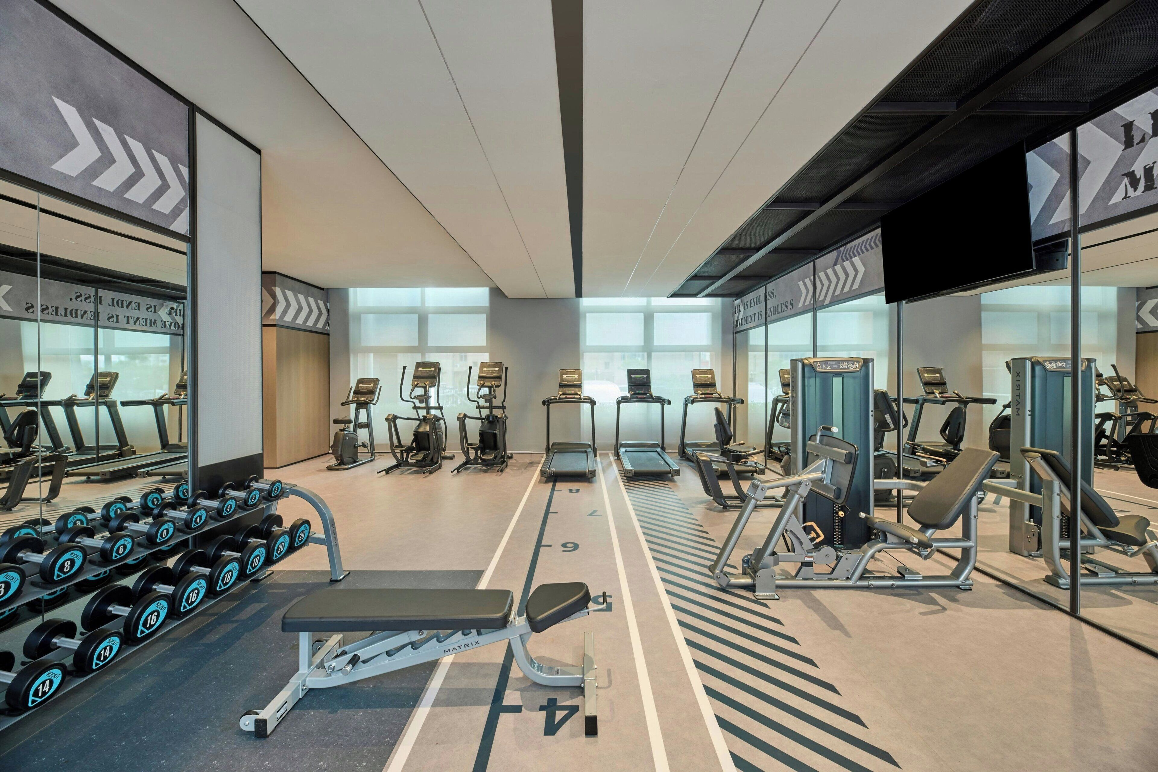 A gym with treadmills, weight machines, and dumbbells.