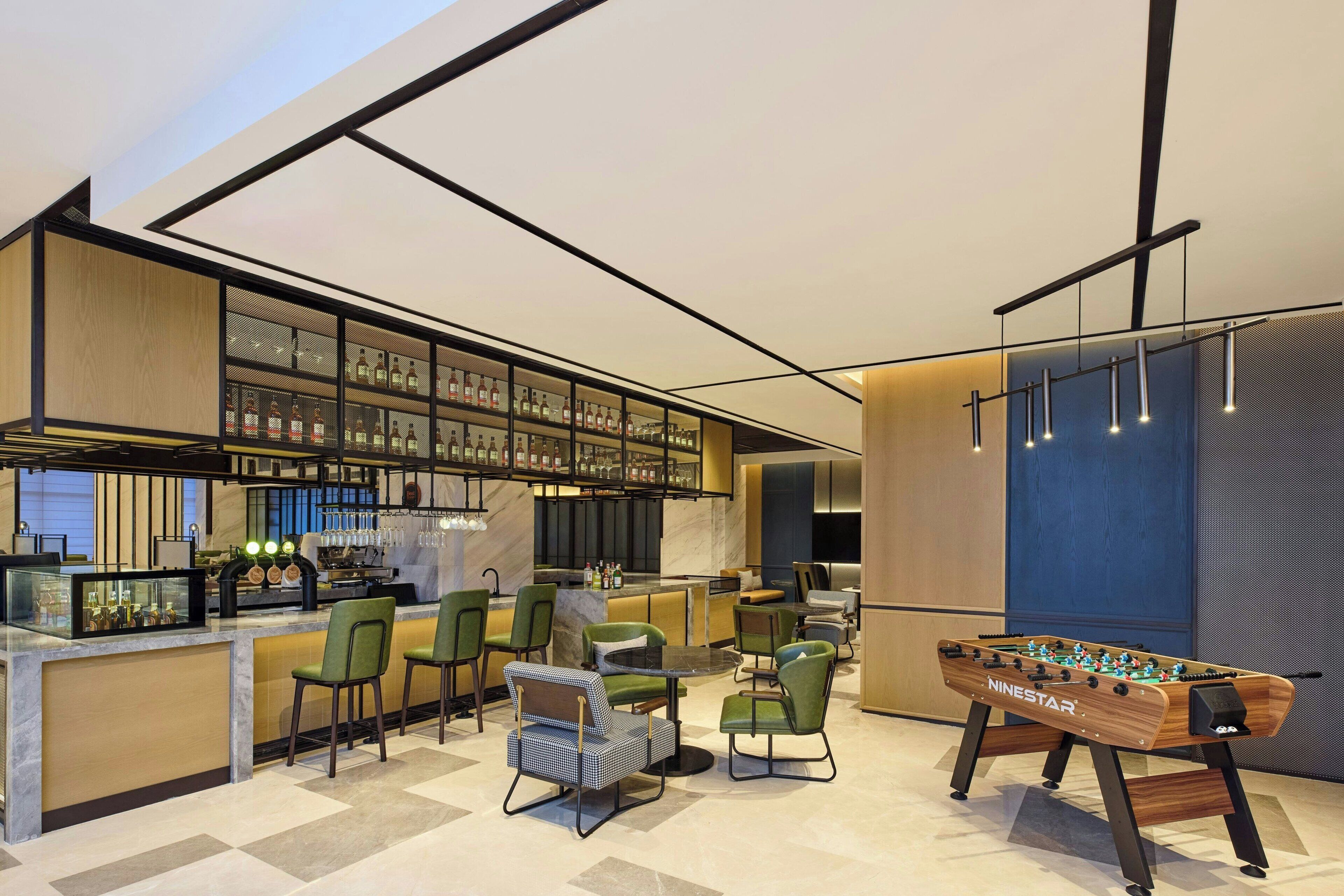 A modern bar area with a foosball table, bar stools, and a liquor display.