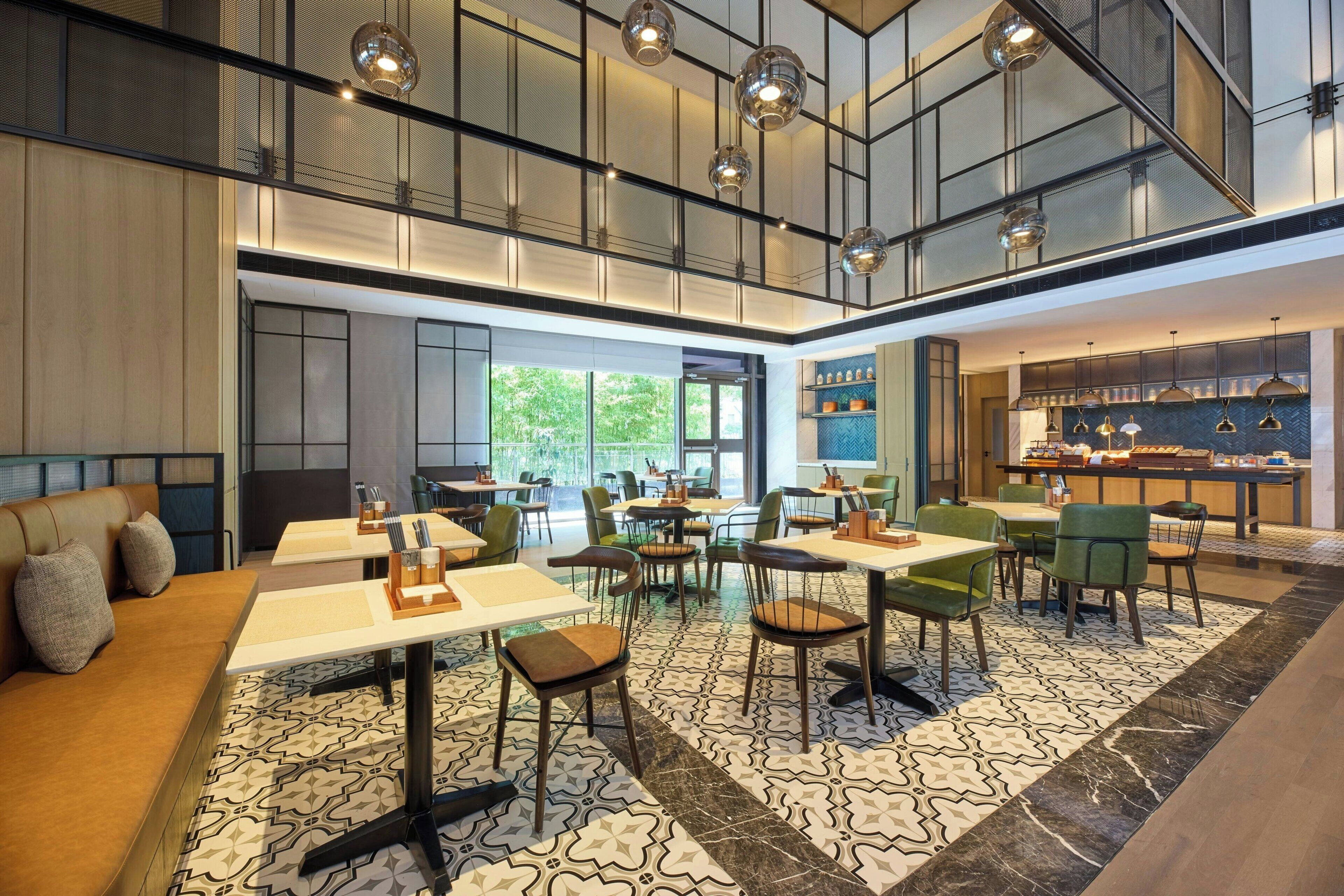 A modern dining area with high ceilings, geometric patterned flooring, and a mix of seating options including tables and chairs.