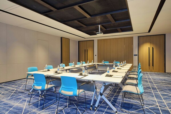 A conference room with a long table, blue chairs, and a patterned carpet.