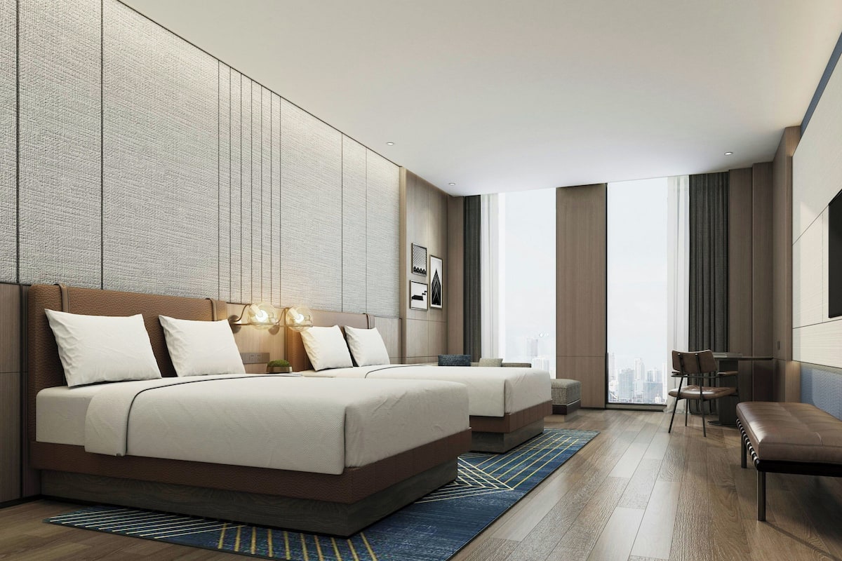 A modern hotel room with a large bed, a desk, and a view of the city.