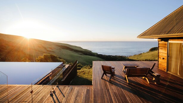 Une terrasse en bois avec vue sur l’océan, une chaise longue et une table.