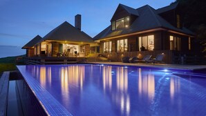 Une maison moderne dotée d’une grande piscine, d’une façade en bois et d’un patio bien éclairé.
