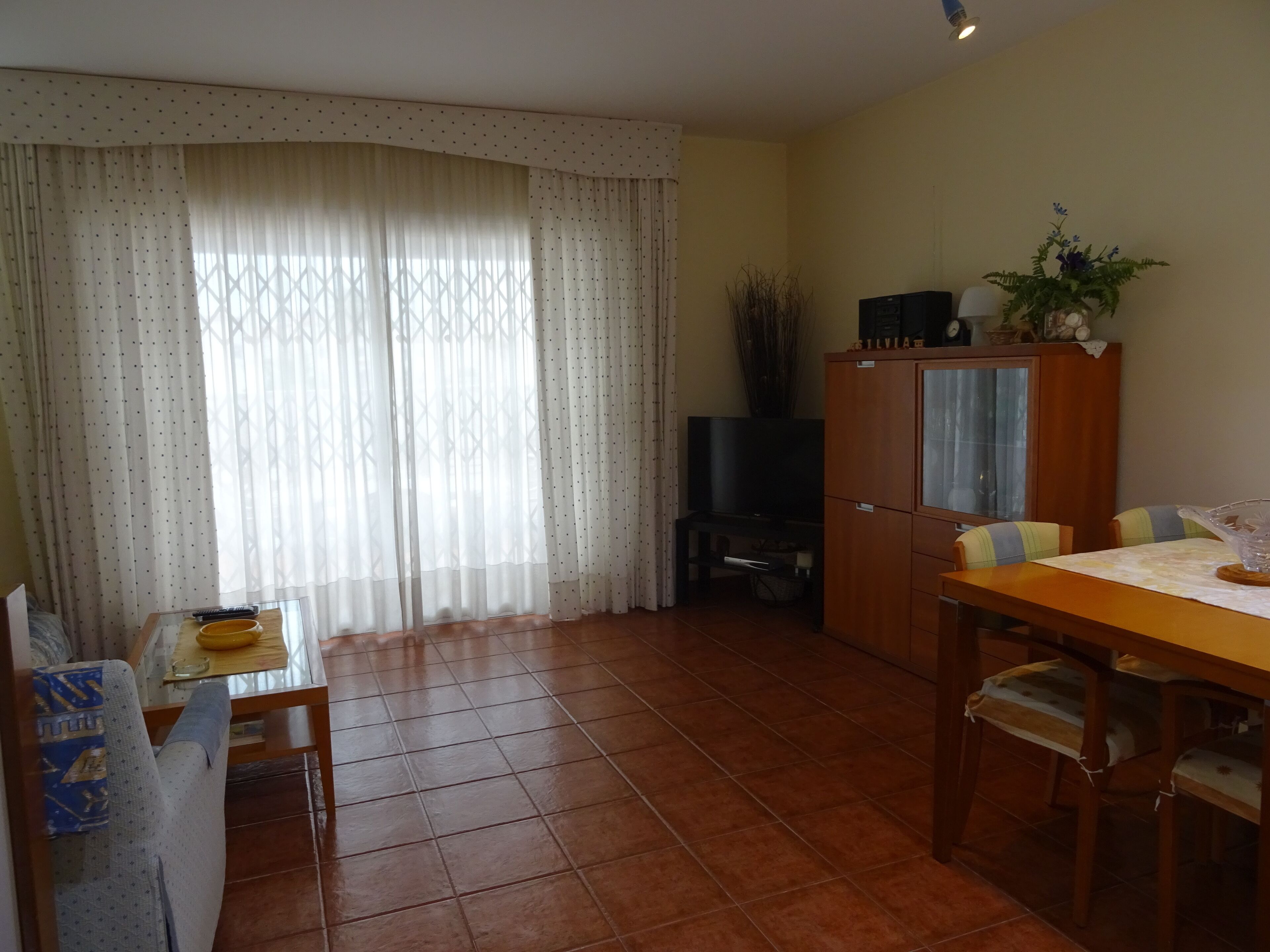 Ein Wohnzimmer mit Fernseher, Schrank und Esstisch mit Stühlen.
