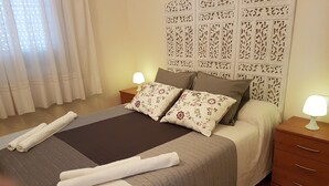 Ein ordentlich bezogenes Bett mit einem gemusterten Bettbezug und Kissen, einer Nachttischlampe und einem dekorativen Kopfteil.