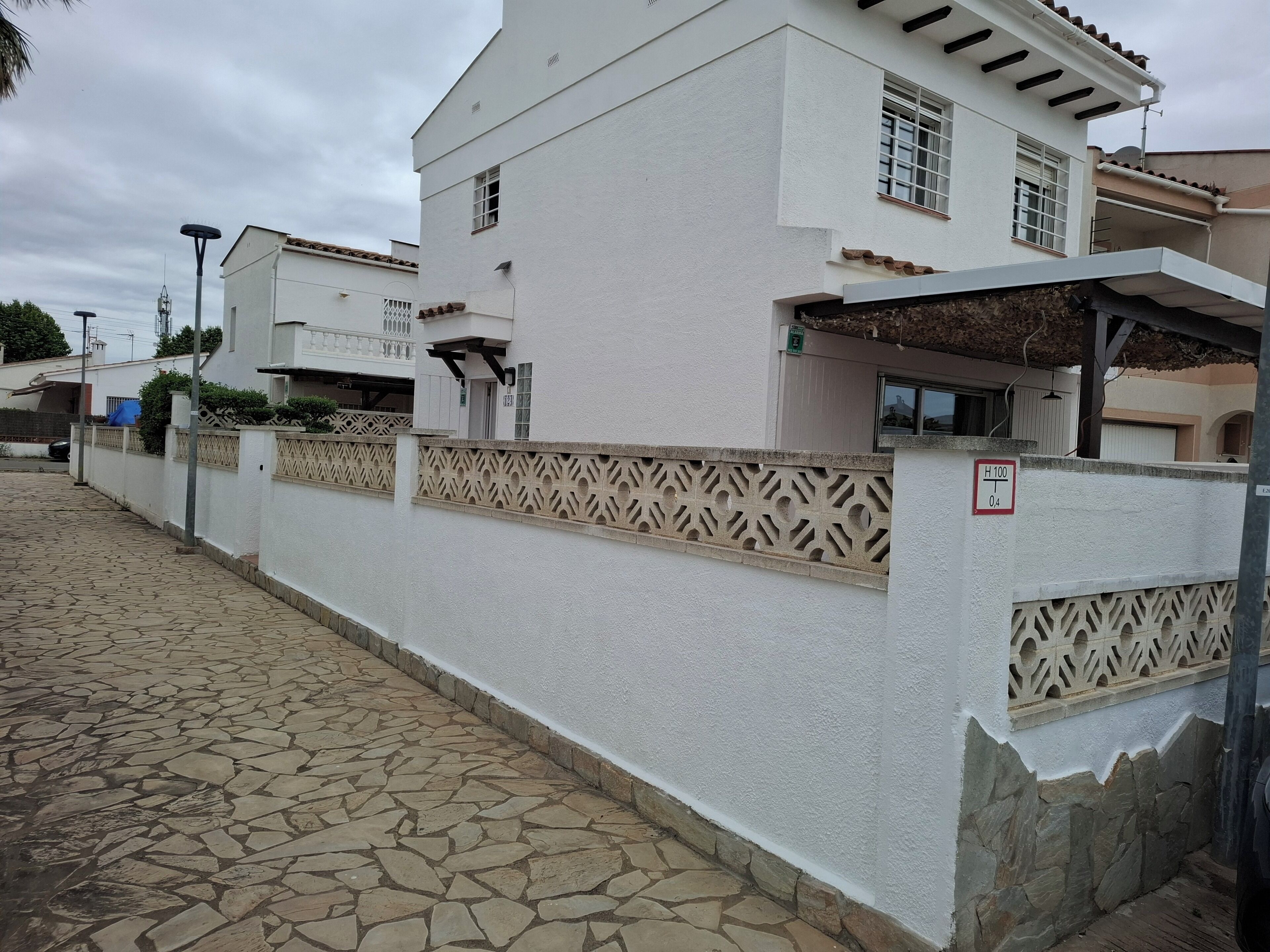 Un edificio blanco con entrada empedrada, cerca decorativa e indicación de restricción de altura.